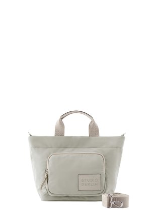 Hellbeige Studio Berlin Handtasche mit oberen Griffen, Front-Reißverschlusstasche und abnehmbarem Riemen, zusammengerollt daneben auf weißem Hintergrund.