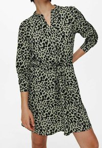 Grünes Kleid mit schwarzem Tiermuster, geknöpfter Kragen, lange Ärmel, tailliert, fließendes Material, knielanges Design.