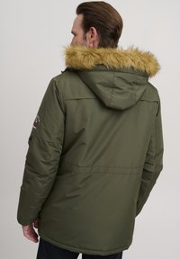 Chaqueta parka verde con capucha forrada de piel sintética, que cuenta con un exterior suave, mangas largas y un emblema en el brazo izquierdo.