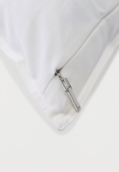Λευκό υφασμάτινο με υφή, με ορατό ασημένιο φερμουάρ και ορθογώνιο έλκτη, που αναδεικνύει τη ραφή στη γωνία και τη λεπτομέρεια του κλεισίματος.