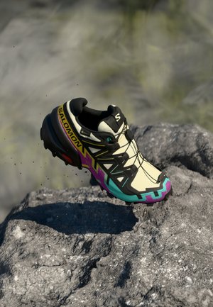 Salomon trail running shoe, beige, with black accents, a multi-colored sole, and a mesh upper. Features a secure lace system and textured grip.