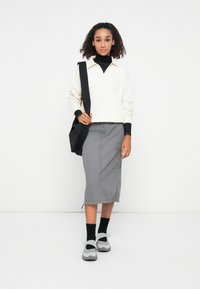 Suéter crema con cuello, camiseta de cuello alto negra, falda gris hasta la rodilla con bolsillos tipo cargo y zapatillas grises con detalles negros.