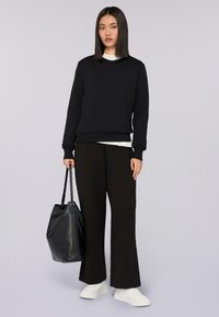 Svart sweatshirt med lång ärm, tillsammans med svarta vida byxor. Tillbehör inkluderar en svart handväska och vita sneakers.