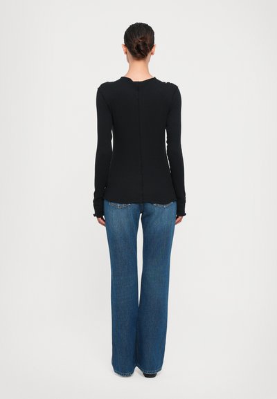 Black long-sleeve top with a rounded neckline and visible seam detailing, paired with wide-leg blue jeans. The fabric appears smooth and stretchy.