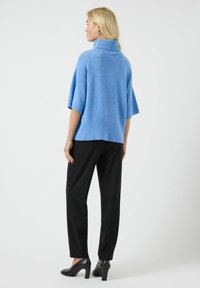 Jasnoniebieski, oversize'owy sweter dzianinowy z wysokim kołnierzem, w połączeniu z czarnymi zwężającymi się spodniami i czarnymi szpilkami. Gładka tekstura.