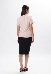 Camiseta de color rosa claro con mangas cortas y cuello redondo, combinada con una falda lápiz negra con un dobladillo con flecos. Textura suave.