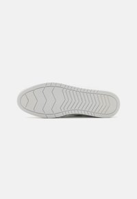 White sneaker sole with zigzag tread pattern, textured rubber material, and slight curvature. Flat, overall design for stability and grip.
