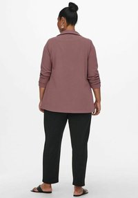 Blazer mauve a maniche lunghe con colletto, tessuto texturizzato e polsini arrotolati, abbinato a pantaloni neri a gamba affusolata e sandali piatti.