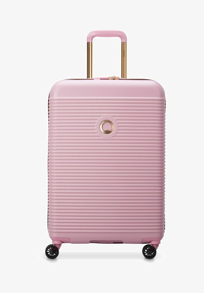 Valise rigide rose avec des rainures verticales, quincaillerie dorée, poignée extensible et quatre roues pivotantes noires pour une maniabilité aisée.