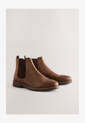 Stivaletti Chelsea in pelle marrone con pannelli elastici laterali, punta arrotondata, tacco basso impilato e dettagli di cuciture lungo la suola.