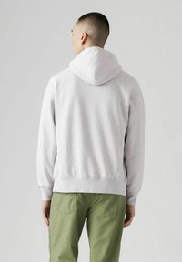 Felpa grigia con cappuccio dalla vestibilità rilassata, caratterizzata da un tessuto strutturato, polsini a costine e una tasca a marsupio. Abbinata a pantaloni cargo verdi.