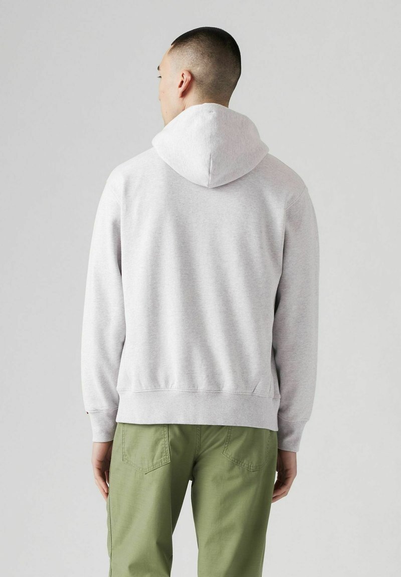 Grauer Kapuzenpullover mit lockerem Schnitt, gefertigt aus strukturiertem Stoff, mit gerippten Bündchen und Kängurutasche. Kombiniert mit grünen Cargohosen.