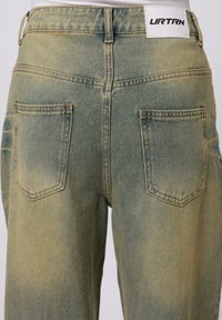 Grønne denimbukser med en falmet vask, to baklommer og et merke på linningen. Rett ben-design, glatt tekstur.