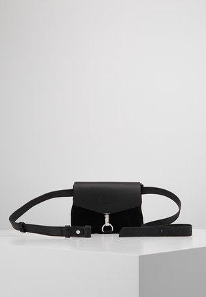 Czarna skórzana torebka na pasek z klapką i srebrną klamrą, położona płasko na białej powierzchni na jednolitym szarym tle.