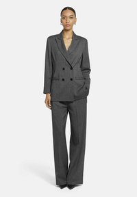 Grijze dubbelzijdige kostuum met een gestructureerd patroon. De jas heeft zwarte knopen en twee voorkruiszakken, gecombineerd met een wijdvallende broek.