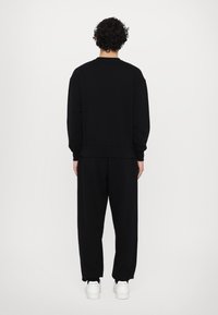 Black sweatshirt and pants set made of soft fabric, featuring a relaxed fit and ribbed cuffs. Paired with white footwear.