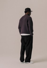 Übergroßer dunkelvioletter Strickpullover über einem weißen Hemd, kombiniert mit schwarzen, weit geschnittenen Hosen und weißen Sneakers. Rückansicht.