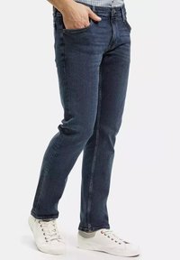 Ciemnoniebieskie dżinsy o dopasowanym kroju, z pięcioma kieszeniami, kontrastowym przeszyciem i prostymi nogawkami. W zestawie z białymi trampkami.