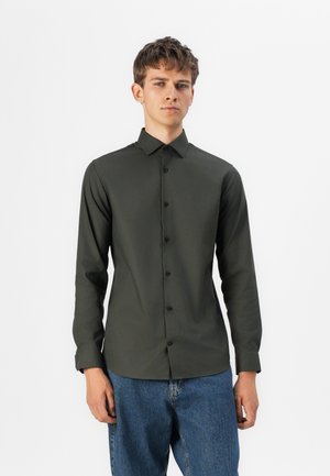 Dunkelgrünes Hemd mit knöpflch, langen Ärmeln, aus glattem Stoff. Verfügt über einen klassischen Kragen und schwarze Knöpfe entlang der Vorderseite. Dazu werden Jeans getragen.