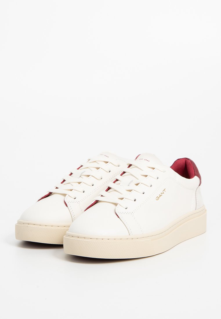 Vita lädersneakers med röd hälaccent, mönstrad sula och sex öglor för snöre. Guldlogotyp på sidan. Platt design.