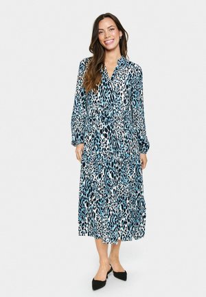 Leopardenmusterkleid in Blau- und Schwarztönen, mit langen Ärmeln, einem V-Ausschnitt und einem gestuften Rockdesign. Schwarze spitze Ballerinas.
