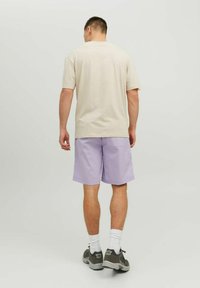 Light beige t-shirt with short sleeves, paired with lilac shorts. Both garments feature a relaxed fit. Shoes are dark gray with white accents.