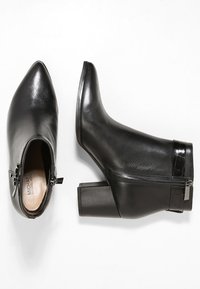Schwarze Leder-Stiefeletten mit spitzem Vorderteil, mittelhohem Blockabsatz, seitlichem Reißverschluss und glänzender Oberfläche. Verfügt über einen subtilen strukturierten Akzent in der Nähe des Absatzes.
