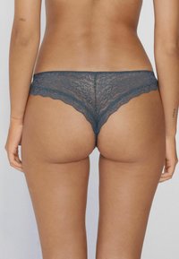 Lace string in diepblauwgroen, met gegolfde randen en een bloemenpatroon. De achterkant biedt minimale bedekking met een gladde textuur.