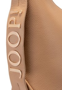 Bretella di pelle con texture marrone chiaro, con lettere in metallo dorato che formano la scritta "JOOP!" attaccate in verticale.