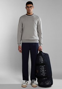 Suéter de algodón gris con cuello redondo, pantalones azul marino y una gran bolsa de deporte negra con una marca blanca. Calzado: zapatillas blancas y beige.
