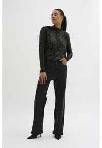 Top lung cu maneci lungi, acoperit cu paiete negre, asociat cu blugi negri largi. Modelul poartă pantofi stiletto negri și cercei mari din cerc. Fundal simplu alb.