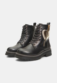 Botas negras de tobillo con parte superior de cuero brillante, acentos dorados, paneles laterales texturizados y cierres de doble cremallera; suela de goma gruesa y detalles de cordones.