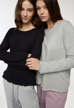 Top a manica lunga neri e grigi con bordi ondulati, abbinati a pantaloni grigio chiaro e rosa con nastri legati. Tessuto dalla texture liscia.