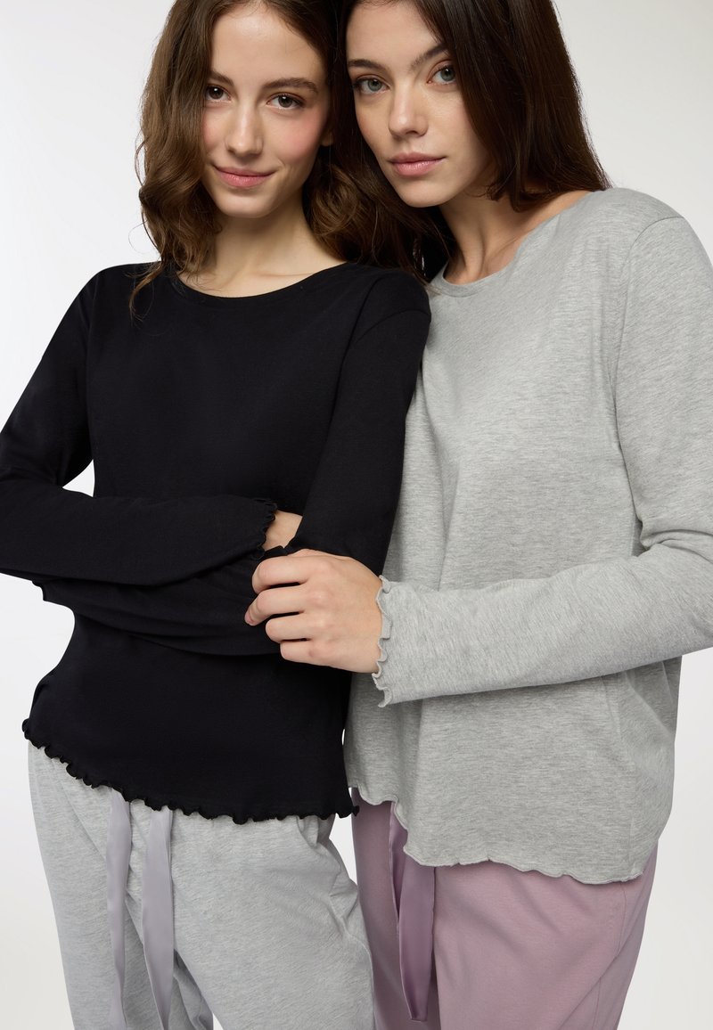 Top a manica lunga neri e grigi con bordi ondulati, abbinati a pantaloni grigio chiaro e rosa con nastri legati. Tessuto dalla texture liscia.