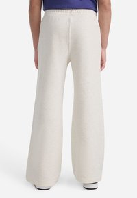 Krémové teplákové nohavice s voľným strihom a elastickým pásom, vyrobené z jemnej látky s jemnou textúrou. Žiadne viditeľné vzory ani akcenty.