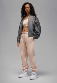 Szara kurtka bomberka, beżowy krótki top, jasnobeżowe spodnie dresowe z kieszeniami oraz białe trampki. Gładki materiał i luźny krój na całej długości.