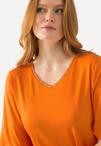 T-shirt arancione a V con maniche corte, caratterizzato da un bordino decorativo attorno al collo. Tessuto morbido e leggero con una vestibilità comoda.