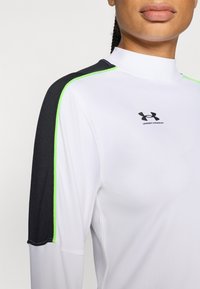 White long-sleeve top with black shoulder and neon green accents, featuring a mock neck and Under Armour logo on the chest.