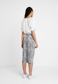 Schwarz-weiße gepunktete Midi-Rock mit hoher Taille und glatter Textur, kombiniert mit einem lockeren weißen T-Shirt und weißen Sneakers.