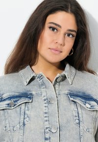 Ljust blå denimjacka med en slitna finish, som har två bröstfickor, silverdetaljer och en klassisk knäppning.