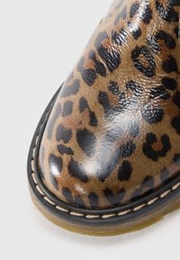 Bottine à imprimé léopard avec une finition brillante, présentant des accents noirs et une semelle cousue. Bout rond et surface texturée.