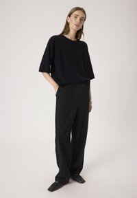Sort oversized t-shirt med korte ærmer, parret med højtaljede sorte vide bukser og sorte slip-on sko. Simpelt design, uden mønstre.