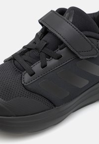 Scarpa da ginnastica nera con punta in mesh, tre strisce di lato, lacci elasticizzati e una fascia in velcro larga sulla parte superiore.
