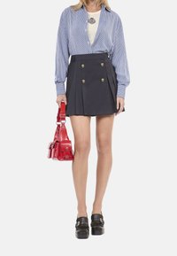 Gestreiftes blaues Langarmshirt, cremfarbenes Unterhemd, marineblaue gefaltete Rock mit goldenen Knöpfen, rotes Handtasche und schwarze Plateauschuhe.