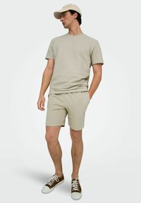 Camiseta de manga corta texturizada en gris claro y pantalones cortos a juego. Combinada con una gorra beige y zapatillas marrones con cordones blancos.