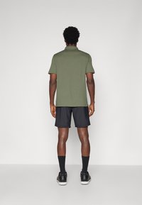 Polo de manga curta verde-escuro, combinado com calções pretos. A camisa tem um design simples e o tecido parece suave e leve.