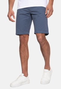 Mørkeblå bomulds shorts med slim fit, opfoldede manchetter, sidelommer og bæltestropper, parret med hvide sneakers.