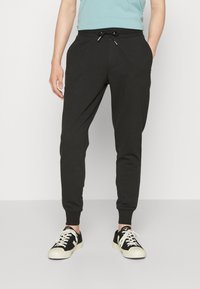 Svarta sweatpants med dragsko i midjan, insvängda ben, sidofickor och ribbade manschetter, kombinerade med svarta och krämfärgade sneakers.