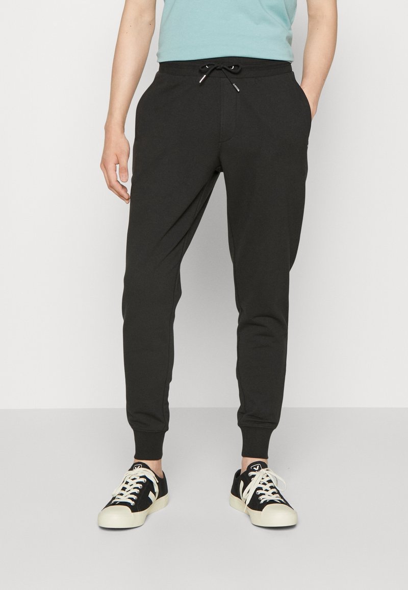 Svarta sweatpants med dragsko i midjan, insvängda ben, sidofickor och ribbade manschetter, kombinerade med svarta och krämfärgade sneakers.