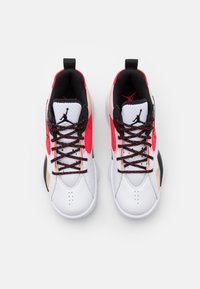 Bílé sportovní boty s černými a červenými akcenty, které mají texturovaný kožený svršek, černé tkaničky a výrazné logo na jazyku.